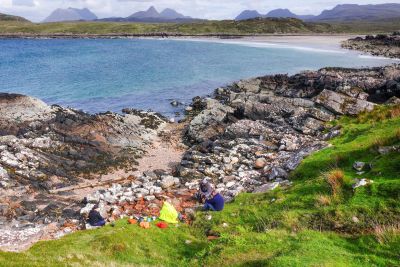 A bay with kayakers and camping equipment in the foreground and mountains in the distance